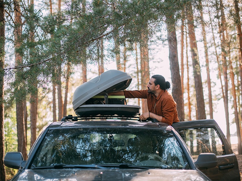 Ein Mann hält mit seinem Wagen im Wald und holt Dinge aus seiner Dachbox.