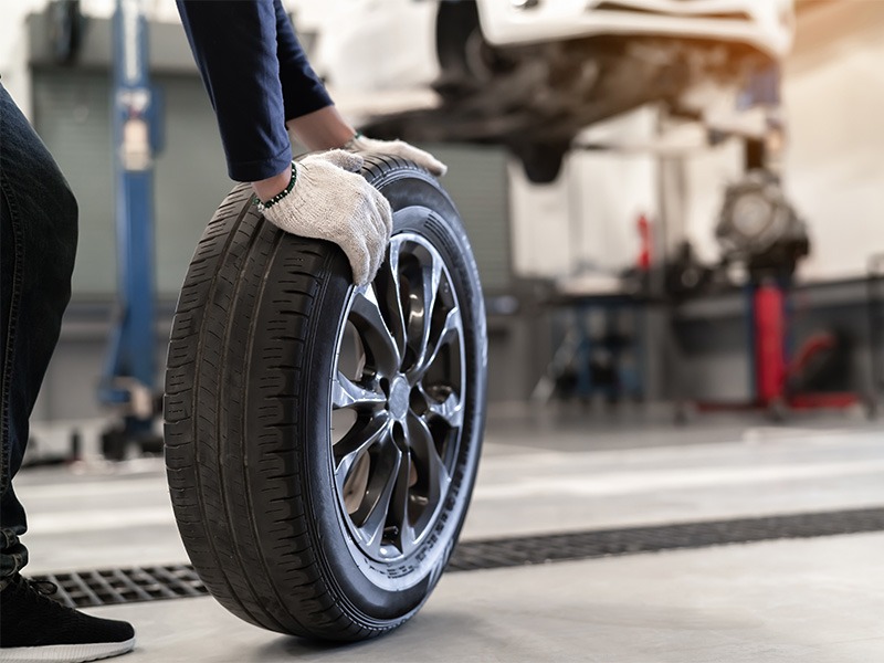 Ein Techniker von Jäckle Automobile rollt einen Reifen zu einem Auto auf der Hebebühne.