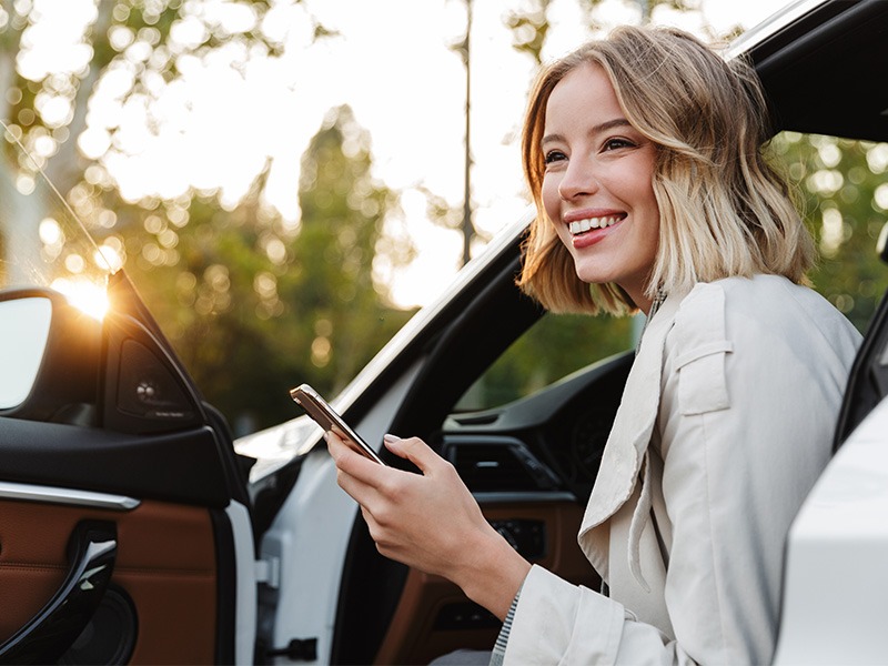 Eine junge Frau steigt freudig aus ihrem neuen Auto aus.