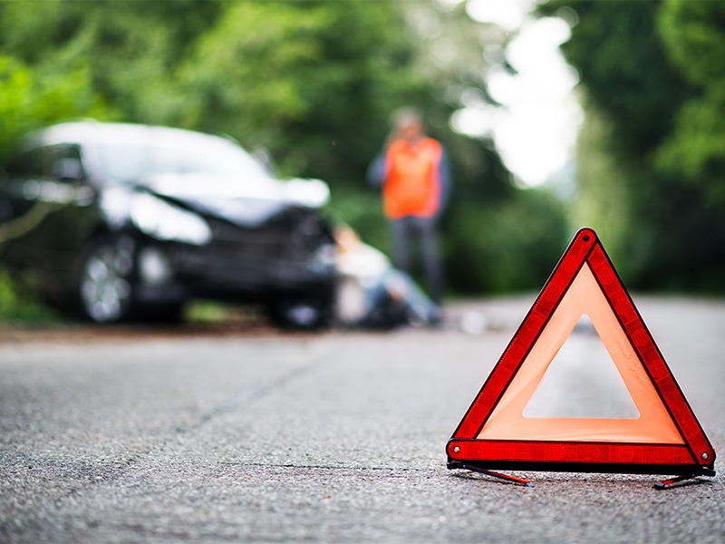 Ein Warndreieck sperrt die Straße. Im Hintergrund erkennt man ein zerdelltes Auto