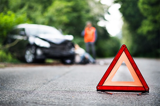 Ein Warndreieck sperrt die Straße. Im Hintergrund erkennt man ein zerdelltes Auto