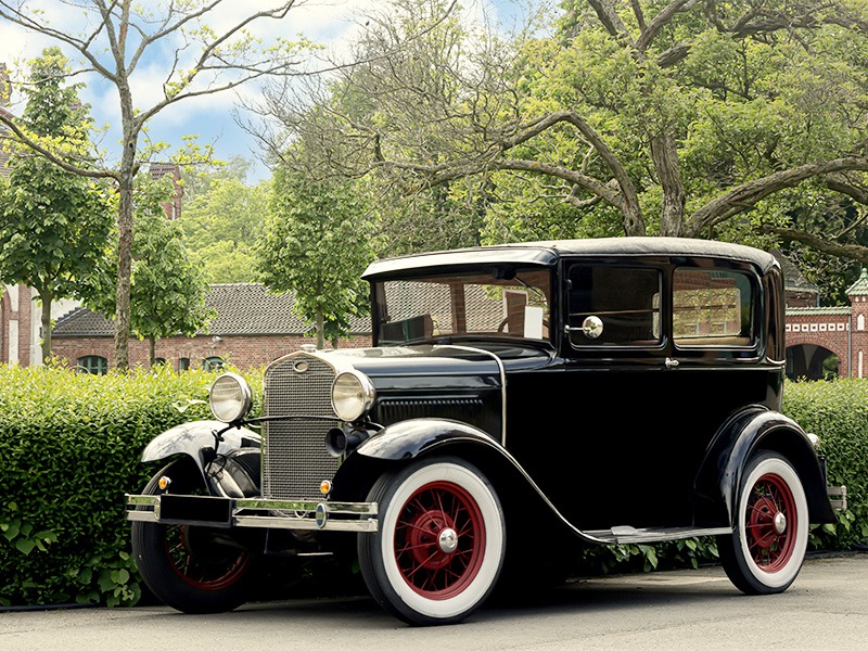 Ein schöner schwarzer Oldtimer steht vor einem Park.