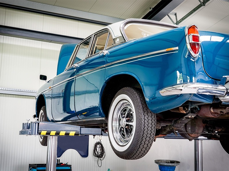 Ein gepflegt aussehender blauer Oldtimer ist auf der Hebebühne und wird ordentlich durchgecheckt.