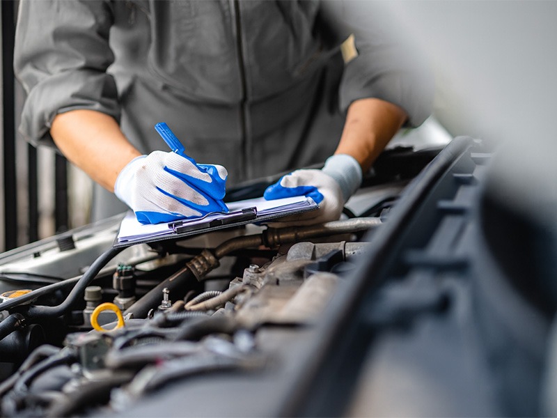 Ein Techniker von Jäckle Automobile erfasst Probleme im Motorraum auf einem Klemmbrett.