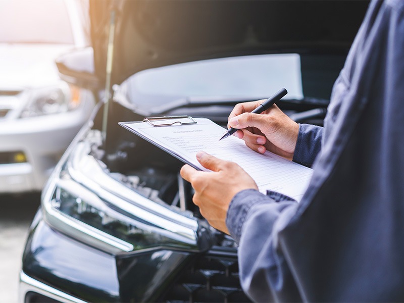 Ein Techniker macht die Hauptuntersuchung an einem Auto und macht Notizen.