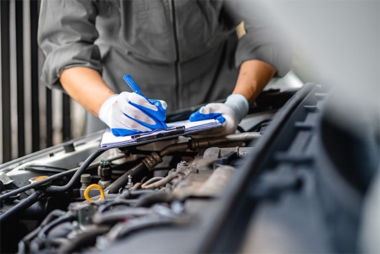 Ein Techniker von Jäckle Automobile erfasst Probleme im Motorraum auf einem Klemmbrett.