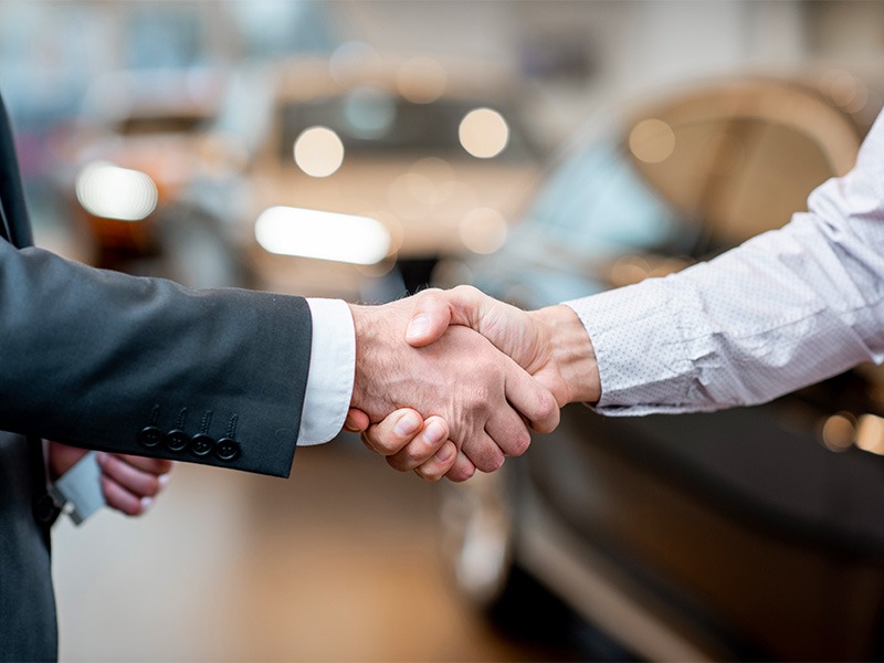 Zwei Männer einigen such auf Autokauf und besiegeln es mit einem Handschlag.