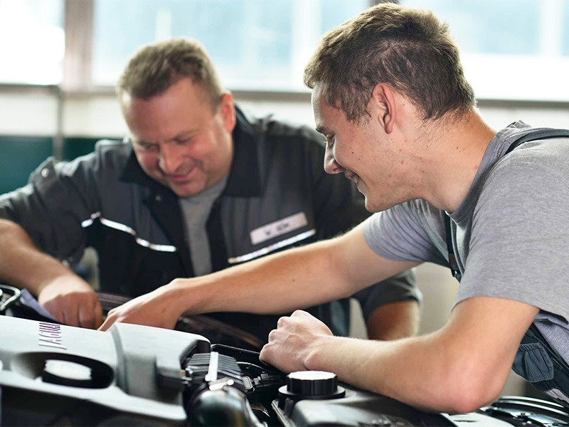 Ein älterer und ein jüngerer Mechaniker von Jäckle Automobile arbeiten am Motorraum eines modernen Autos.